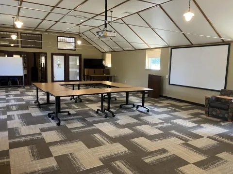 Image of the community room with tables, chairs, projector and screen visable