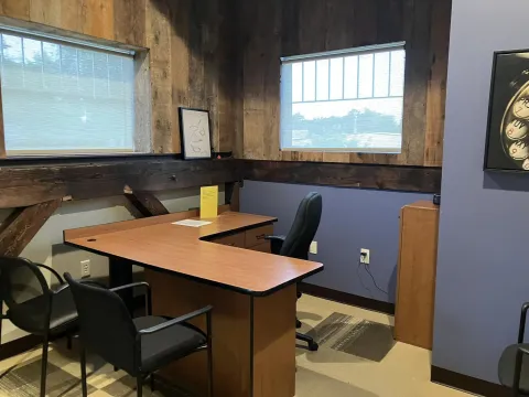 Photograph of Study Room A. The L shaped desk is visible as well as two windows, three chairs and a photograph on the wall.