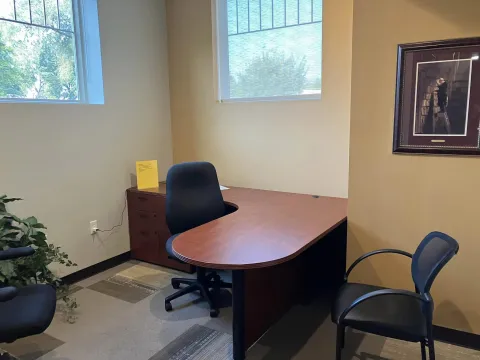 Photograph Study Room D. The L shaped desk can be seen, along with three chairs, two windows and a picture on the wall.