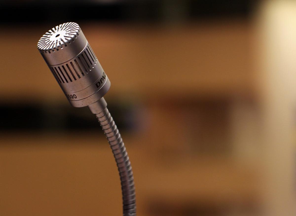 Close up of a silver gooseneck microphone. Background out of focus brown.